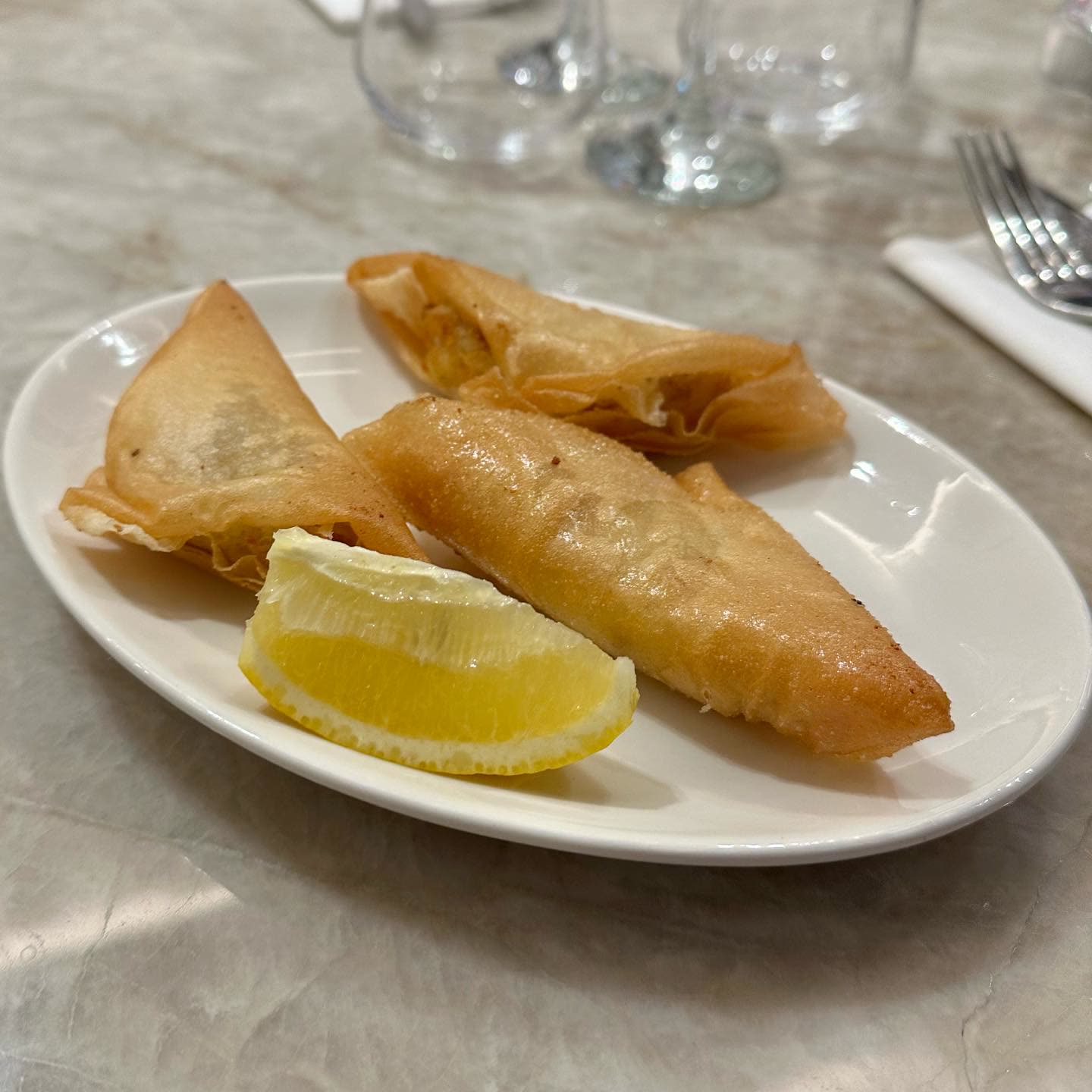 Trois briks dorées servies sur une assiette blanche avec une tranche de citron