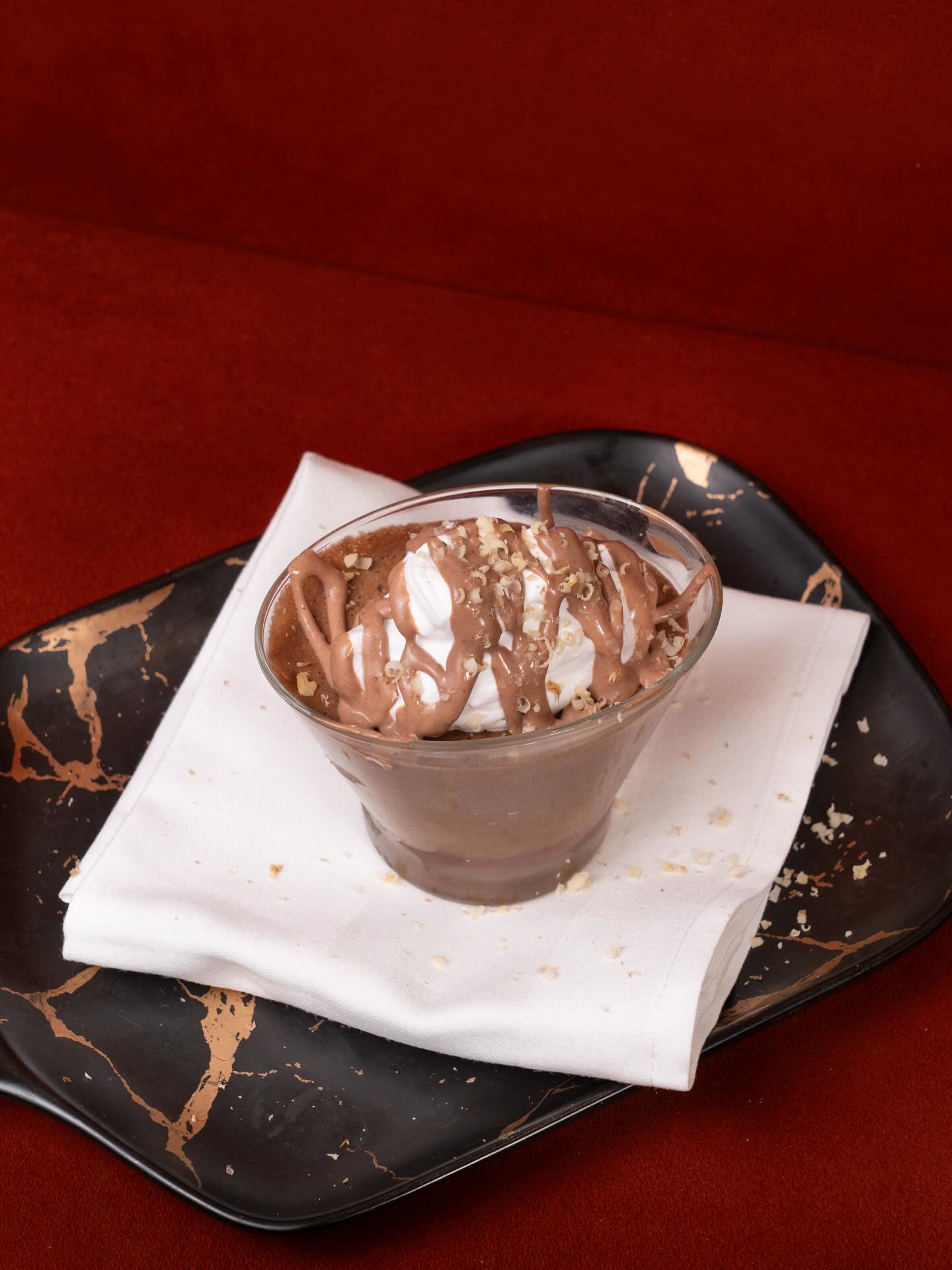 Un dessert au chocolat et à la crème servi dans un verre sur une serviette blanche