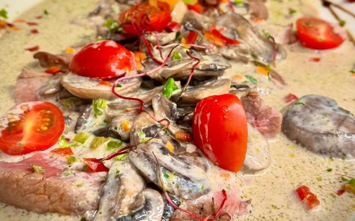 Tranches de viande servies dans une sauce crémeuse avec des champignons et des tomates cerises