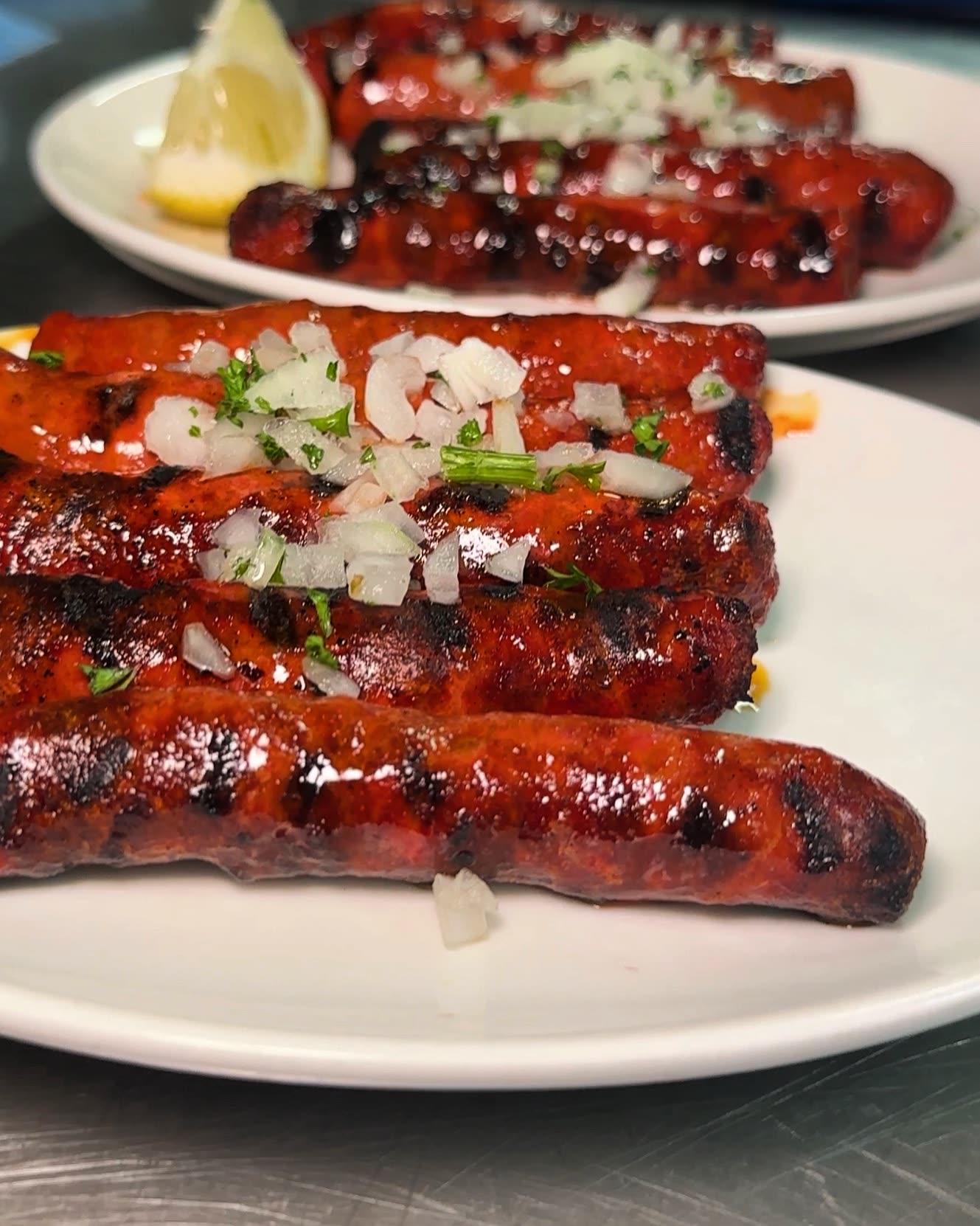 Plusieurs saucisses grillées servies sur une assiette blanche avec des oignons et du persil