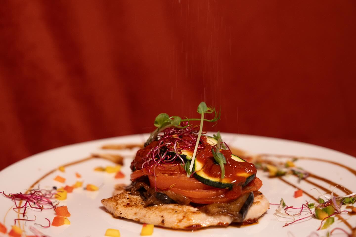 Une pièce de viande grillée garnie de légumes et de micro-pousses sur une assiette décorée