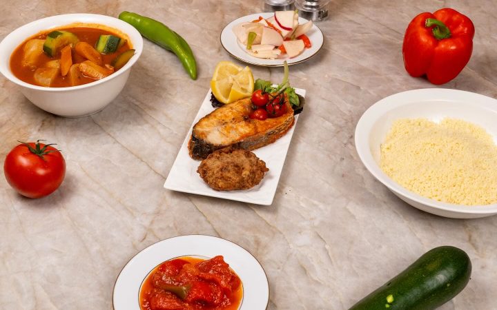 Plusieurs petits plats de mezzés et légumes frais sont disposés sur une table en marbre