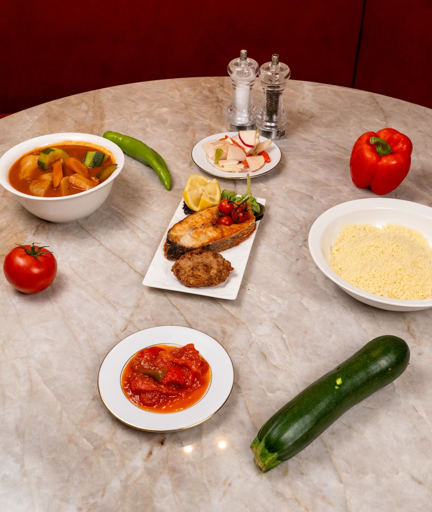 Plusieurs petits plats de mezzés et légumes frais sont disposés sur une table en marbre