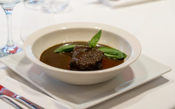 Un morceau de viande dans une sauce brune servie dans un bol blanc