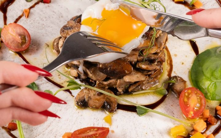 Une assiette composée de champignons, d'un œuf au plat et de tomates cerises avec un filet de sauce brune