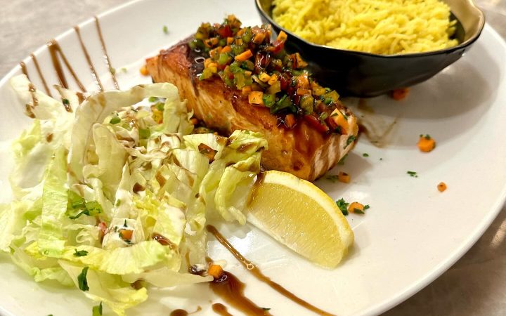 Un pavé de saumon grillé accompagné de riz jaune et d'une salade verte sur une assiette blanche