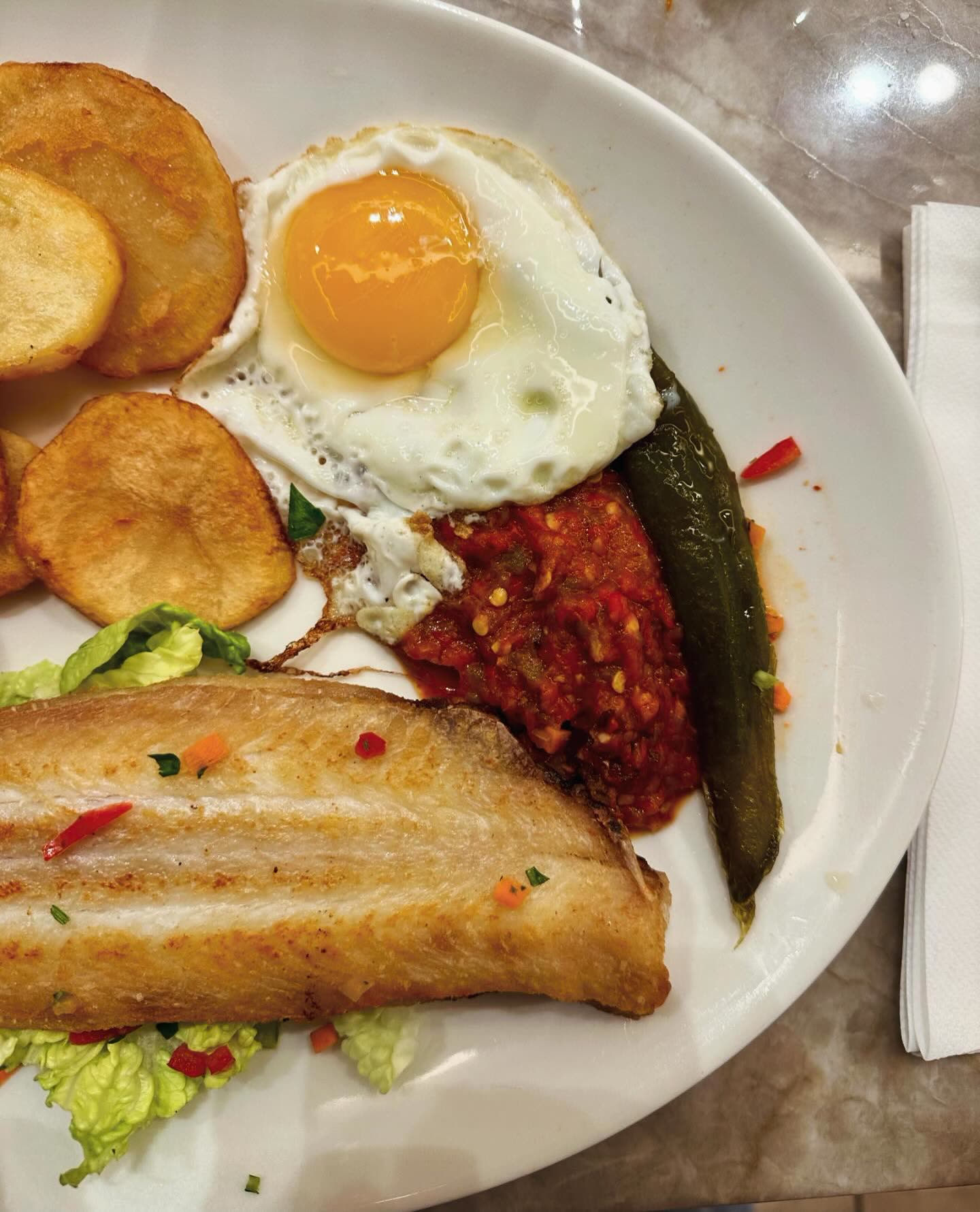 Un filet de poisson grillé accompagné d'un œuf au plat, de pommes de terre et de légumes