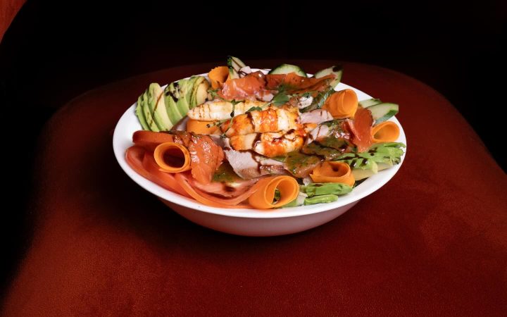 Une salade composée de poisson, crevettes et avocat servie dans une assiette blanche sur un fond sombre