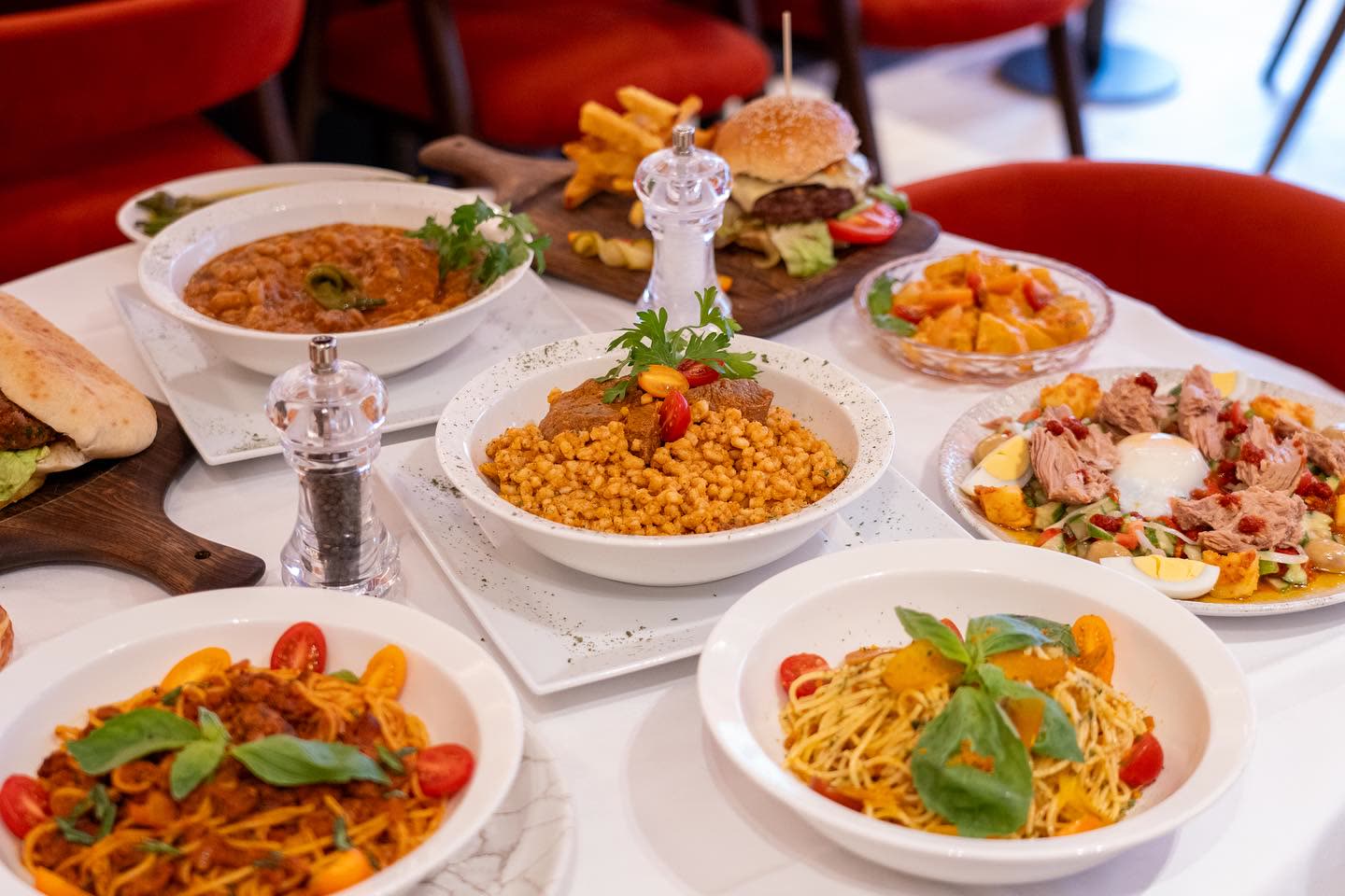 Une table garnie de divers plats tunisiens et internationaux comme du couscous, des pâtes et un burger