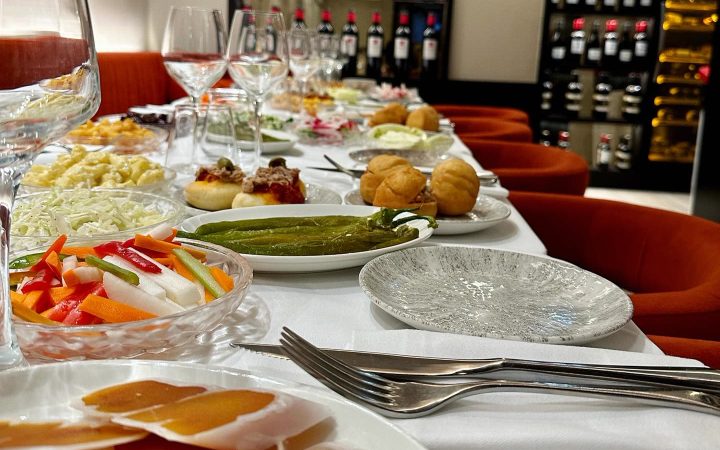Une table richement garnie de diverses entrées et plats dans un restaurant avec une cave à vin en arrière-plan