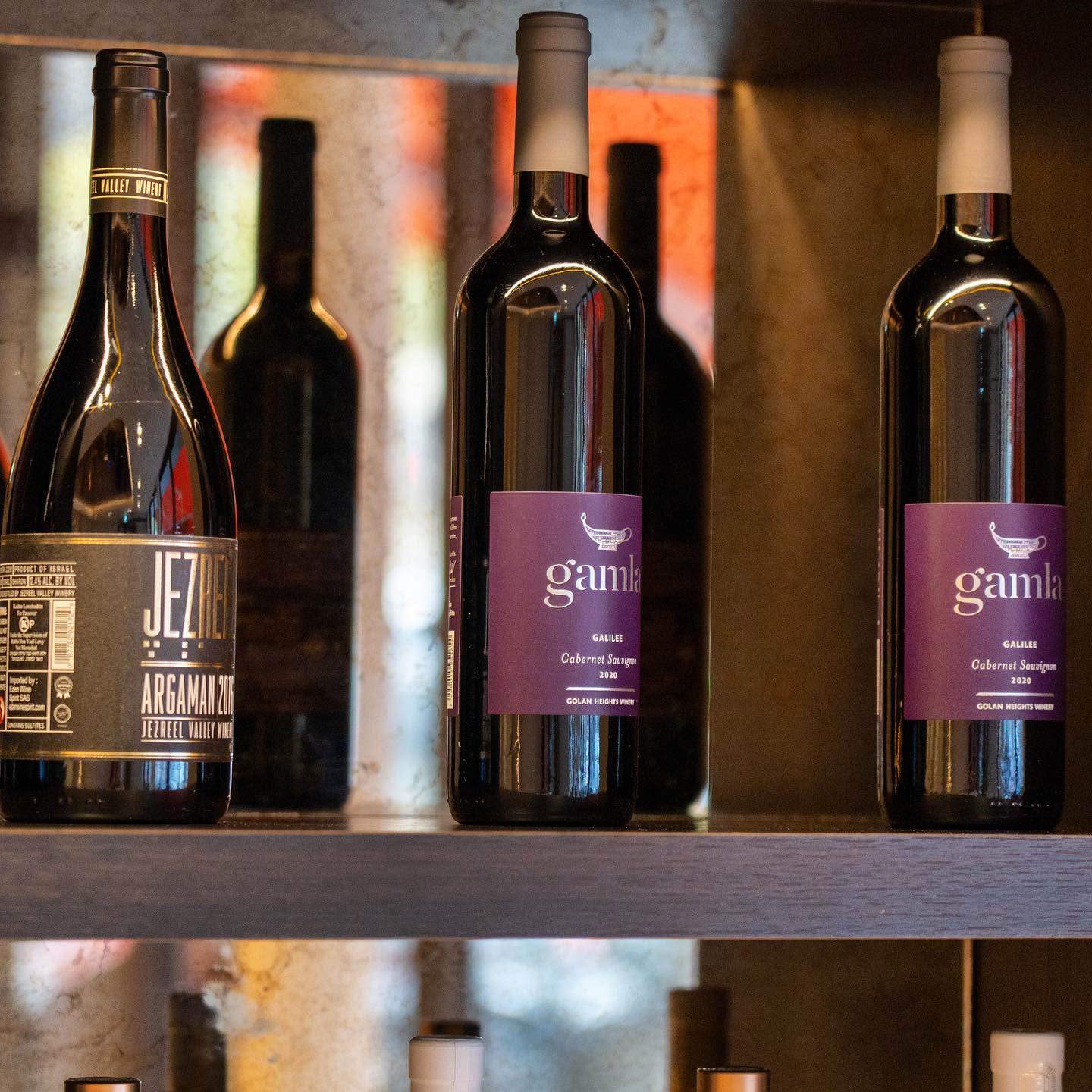Trois bouteilles de vin rouge sont alignées sur une étagère de restaurant