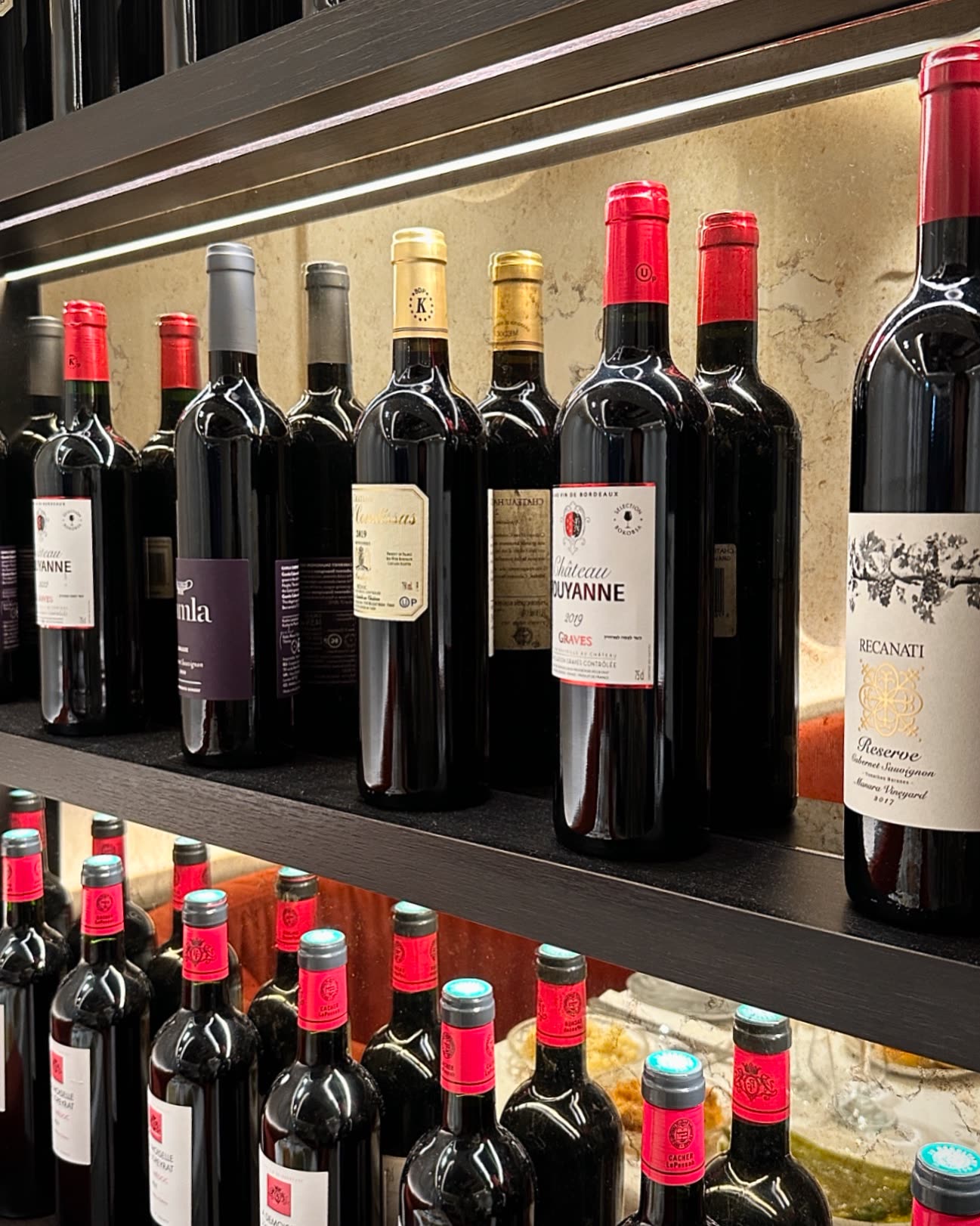 Plusieurs bouteilles de vin rouge sont alignées sur des étagères éclairées dans un restaurant