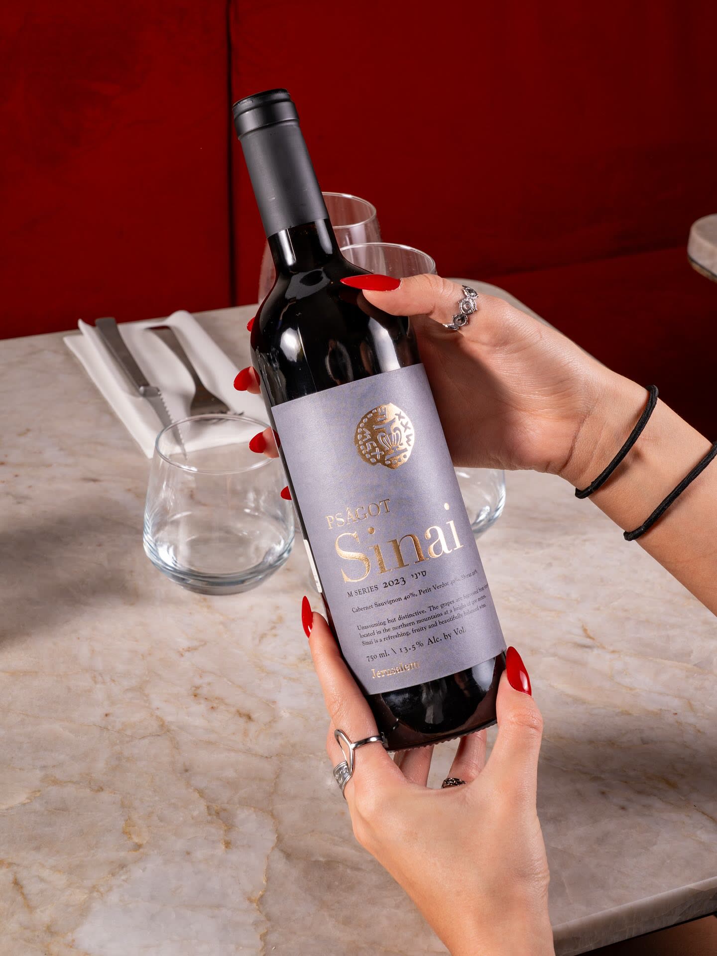 Une personne tient une bouteille de vin rouge Sinai devant des verres sur une table